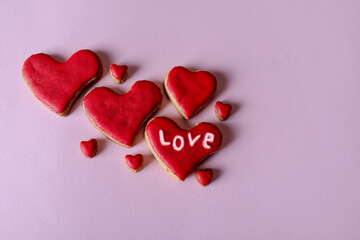 Cute hand made red cookies in the shape of a heart with word love isolated on purple background with copy space for text or design. Valentines day and love concept