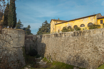 Obraz premium Part of the castle of the city of Brescia on a sunny winter day. A look from the bridge. Castello di Brescia, Lombardy, Italy. Medieval castle with battlements, a tower, drawbridge and ramparts. 