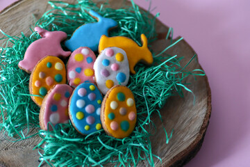 Cute homemade colorful cookies in the shape of eggs and rabbit on log and grass. Easter holiday concept food decoration