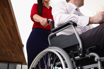 Fototapeta na wymiar Woman rolls man in a wheelchair in office. Businessmen with disabilities concept