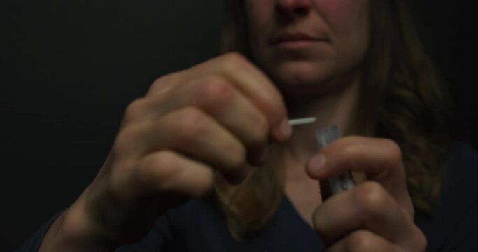 A young woman is putting a corona virus test swab in a container to be sent off for analysis