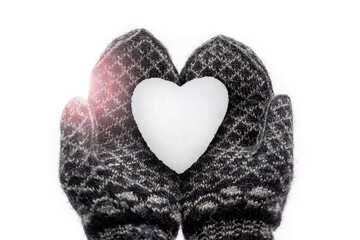 Hände in Handschuhen mit Norweger Muster halten ein Herz aus Schnee, Schneeherz im Gegenlicht mit Blendenflecken. Geringe Schärfentiefe