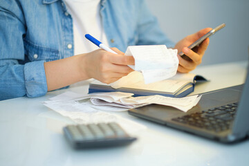 woman using a pen writing on bank account book while holding the bills to calculate in living room at home. Expenses, account, taxes, home budget concept