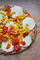Colorful raw pizza before baking with mozzarella cheese, corn, pesto and cherry tomatoes. Frozen, unbaked, gluten free pizza placed on a baking sheet before putting it in the oven. Top view.