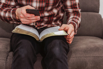 Man holding the smartphone in his hands while reading the bible.