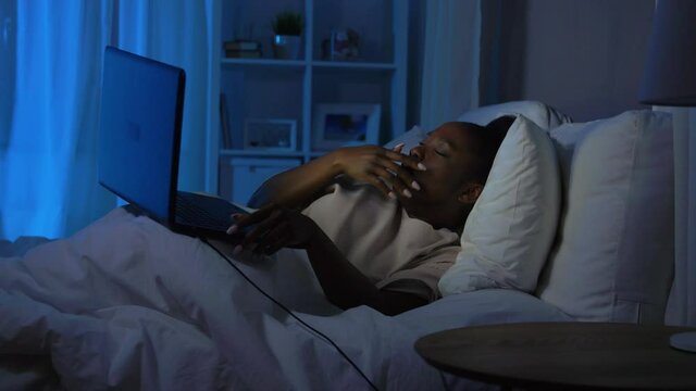 technology, bedtime and people concept - tired young african american woman closing laptop computer and going to sleep in bed at home at night