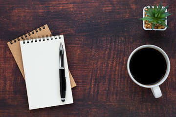 Top view of open school notebook with blank pages, coffee cup and pen for taking write notes on wood table background. Flat lay, creative workspace office. Business-education concept with copy space.