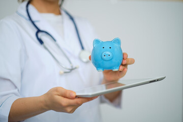 Female Doctor with Stethoscope Holding Piggy Bank and tablet computer. Perfect medical service in clinic. Modern medicine, medic data and healthcare concepts.
