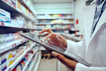 Closeup of hands of young female pharmacist checking inventory in medical store using digital tablet - 414670788