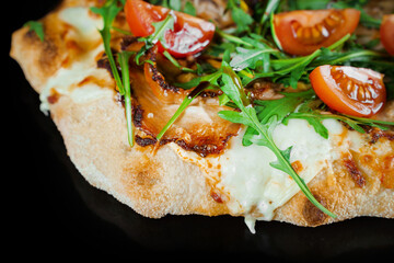 Pinsa romana gourmet italian cuisine on black background. Scrocchiarella traditional dish. Food delivery from pizzeria. Pinsa with meat, arugula, tomatoes, cheese.