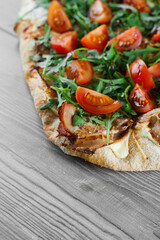 Scrocchiarella gourmet italian cuisine on grey wooden background. Pinsa romana traditional dish. Food delivery from pizzeria. Pinsa with meat, arugula, tomatoes, cheese.