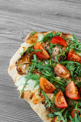 Scrocchiarella gourmet italian cuisine on grey wooden background. Pinsa romana traditional dish. Food delivery from pizzeria. Pinsa with meat, arugula, tomatoes, cheese.
