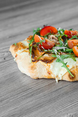 Scrocchiarella gourmet italian cuisine on grey wooden background. Pinsa romana traditional dish. Food delivery from pizzeria. Pinsa with meat, arugula, tomatoes, cheese.