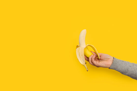 Mano femenina sosteniendo un pl&aacute;tano fruta sobre un fondo amarillo liso y aislado. Vista de frente. Copy space. Concepto de nutrici&oacute;n, salud.