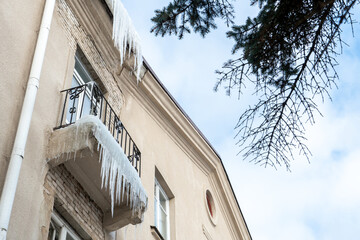 Fototapeta na wymiar Large icicles hang from the roof of the building and from the balcony. Winter city landscape. The fall of icicles carries a danger to people's lives.
