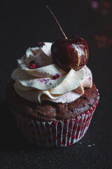 Chocolate cupcake with whipped cream and golden cherry on dark background