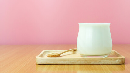 Pure yogurt on a wooden table and pink background.