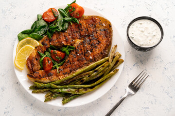 grilled salmon steak, asparagus and fresh spinach with tomatoes on a white plate on a light background