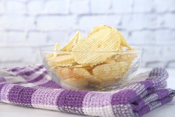Bowl with tasty potato chips on wooden background .