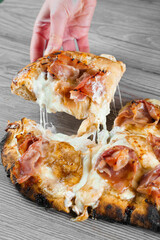 Mozzarella stretching cheese on pinsa romana gourmet italian cuisine. Food delivery from pizzeria. Junk food. Scrocchiarella with pear, cheese, prosciutto on grey wooden background.