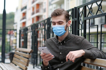Fototapeta na wymiar Handsome man in blue medical protective face mask looks in his smartphone