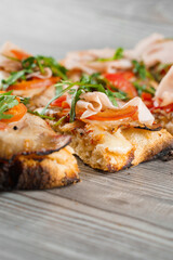 Pinsa romana cut into pieces portions for one person. Food delivery from pizzeria. Pinsa with meat, arugula, cheese. Scrocchiarella gourmet italian cuisine on grey wooden background.