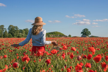 beautiful woman is walking through a poppy field at sunset. Enjoing the nature and freedom.