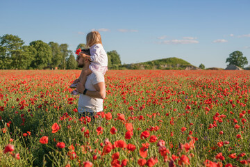 Fototapeta premium Happy father and daughter walk in the summer field of poppies. Nature beauty, blue sky and field with red poppies. Outdoor lifestyle. Freedom concept.
