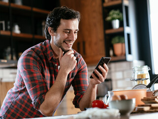 Handsome man preparing breakfast at home. Young man drinking coffee and using the laptop