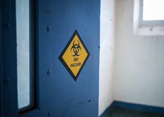 Warning danger biohazard sticker on prison cell blue open door sunlight in window of high security run down jail immigration detention centre in England