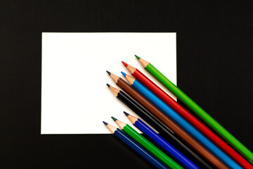 Several colored pencils on a white sheet. Black background.