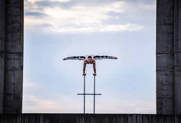 Flexible male circus Artist keep balance on hands in the concrete structure on sky background with...