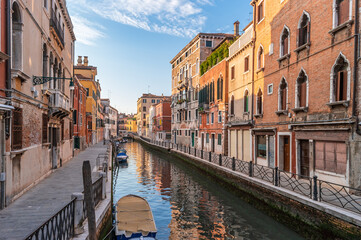 Fototapeta na wymiar View of cozy street and calm canal with boats along brink. The residential area of Venice, Italy.