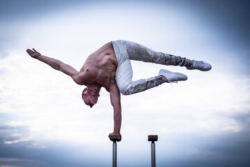 Circus artist keeps balance on one hand on the cloudy sky background. Concept of handstand, performing and art