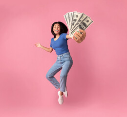 Young asian woman holding bunch of money while jumping