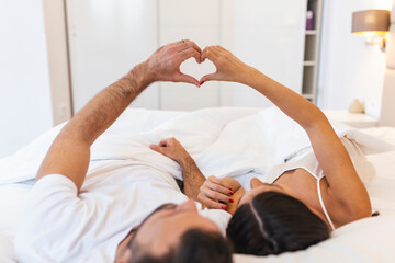 Obraz na płótnie Canvas Couple Lying On Bed Forming Heart Shape With Hand