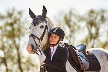 Beautiful horse rider girl stands near a horse on a farm   