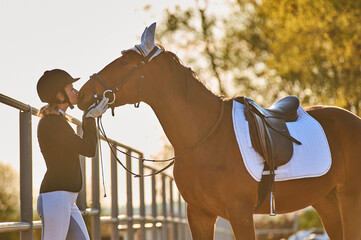 Beautiful horse rider girl stands near a horse on a farm   