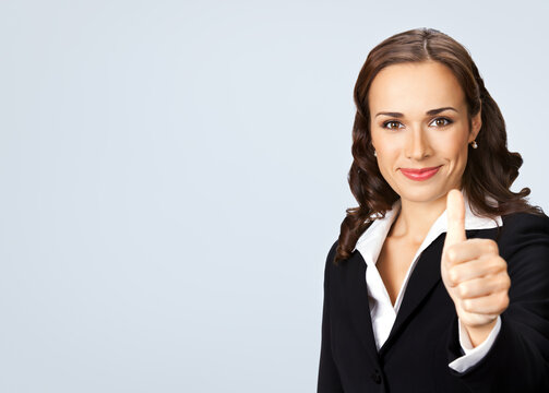 Smiling brunette businesswoman in black confident suit, showing thumbs up gesture, isolated over grey background. Business success concept. Copy space for text.