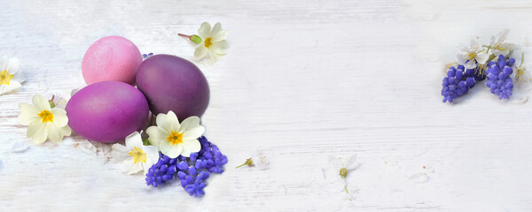 easter eggs painted in pink and purple on a table among spring flowers and petals