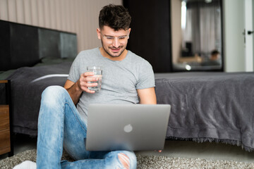 Businessman working on laptop computer sitting at home while drinking water from glass. Man working on laptop computer sitting on the floor with his diary and official papers.