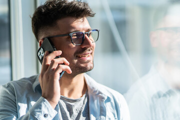 Handsome young man talking on phone relaxed near window in a morning