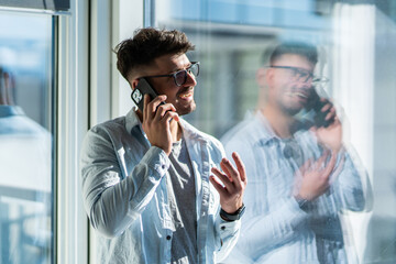 Handsome young man talking on phone relaxed near window in a morning