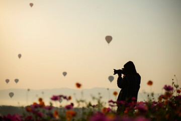 Lifestyle traveler women raise hand feeling good relax and happy freedom and see the fire balloon outdoors the nature tea and cosmos farm in the sunrise morning. Travel and summer Concept