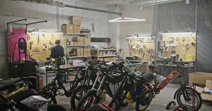 Large workshop business eco project for the production of electric bicycles. A man works on the background of a large range of electric bicycles eco bicycles in a large room with artificial lighting