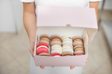 Close up top angle view of colorful macarons in a gift box in hands of female confectioner. Traditional french dessert macaroons in a rows in paper present box