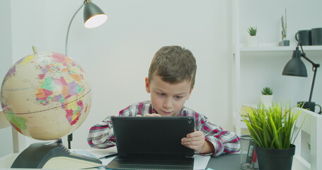 Kid boy doing school homework with tutor. Child learning foreign languages using tabletPC. E...