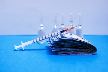 Syringe to take advantage of the coronavirus, covid or flu vaccine on top of a bundle of money in...
