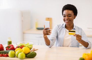 Obraz premium Woman Using Phone Grocery Shopping Application Holding Credit Card Indoor