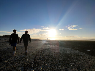 Silhouette of two man walking on a pebble beach